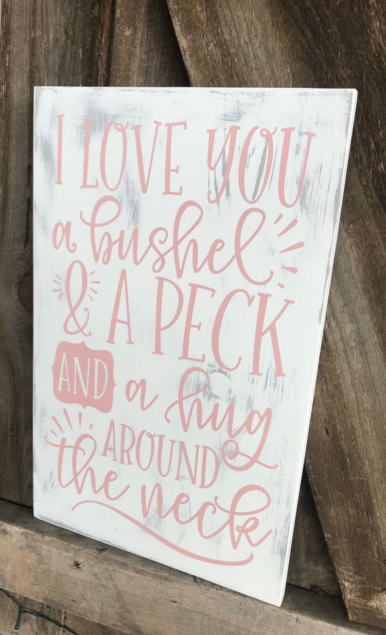 May include: White wooden sign with distressed paint featuring the text "I love you a bushel & a peck and a hug around the neck" in pink lettering.
