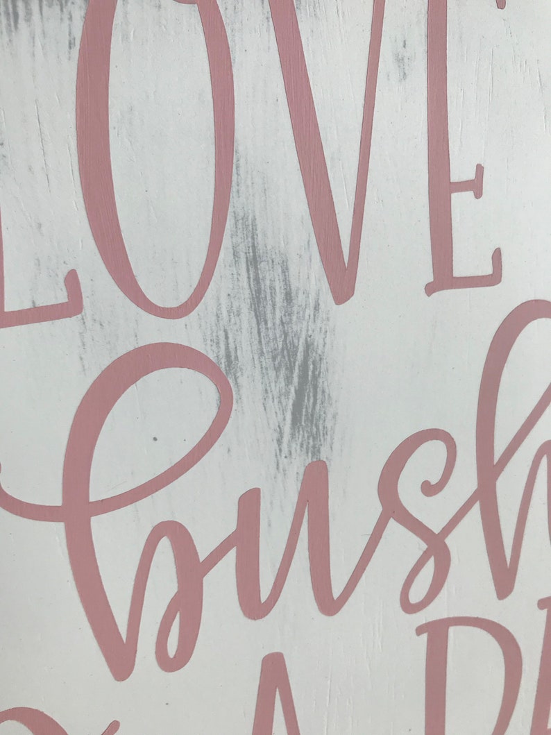 May include: A white wooden sign with the words "Love, bush, and dreams" written in pink cursive lettering.