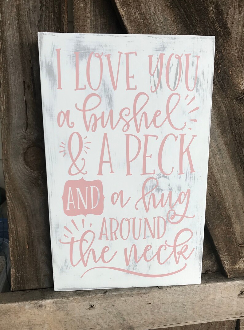 May include: White wooden sign with pink lettering that reads "I love you a bushel & a peck and a hug around the neck".