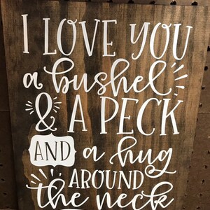 May include: A wooden sign with white lettering that reads "I love you a bushel & a peck AND a hug around the neck".