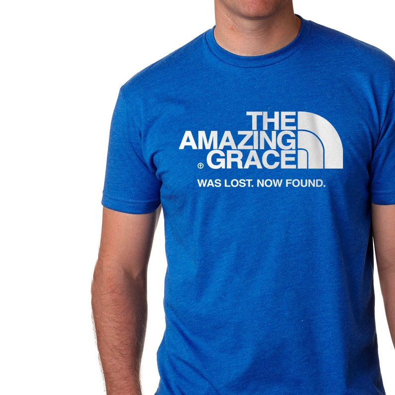 Puede incluir: Una camiseta azul real con un dise&ntilde;o gr&aacute;fico blanco que dice "The Amazing Grace Was Lost. Now Found." El dise&ntilde;o gr&aacute;fico es una parodia del logotipo de North Face.