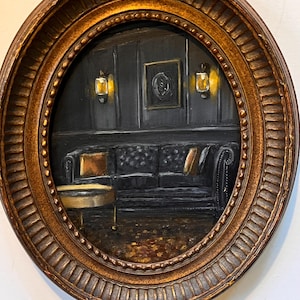 May include: An oval-shaped painting in a gold frame depicts a dimly lit room with a black leather sofa, a small table, and wall sconces. The artwork has a vintage aesthetic, with warm lighting and a detailed interior scene.