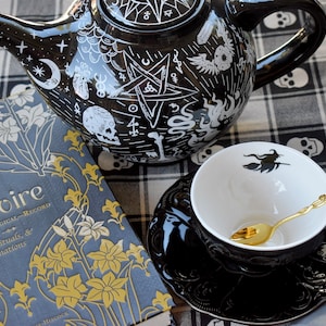 Tazza da tè e piattino in stile gotico vittoriano con tema Halloween, in porcellana nera goffrata, con cucchiaio placcato oro. Bustina da tè a tema. Fornita con scatola regalo.