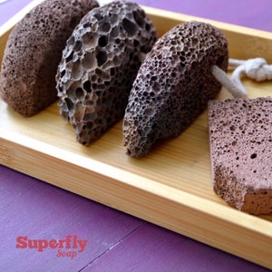 May include: Four brown pumice stones on a wooden tray. The stones are rough and have a porous texture. The tray is made of light brown wood and has a smooth surface.