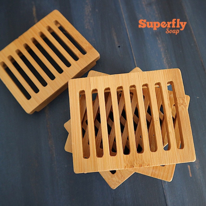 May include: Three wooden soap dishes with a slatted design. The dishes are stacked on top of each other. The top dish has a more intricate design with criss-crossed slats. The text "Superfly Soap" is visible in the top right corner of the image.
