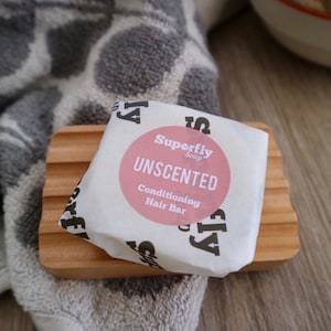 Op de afbeelding: Een witte, ongeparfumeerde conditionerende haarzeep in een witte verpakking met zwarte tekst die "Superfly Soap" en "UNSCENTED Conditioning Hair Bar" zegt.