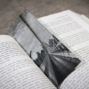 Puede incluir: Una fotografía en blanco y negro de un puente con un largo camino recto que conduce al horizonte. El puente está hecho de metal y tiene una serie de arcos.
