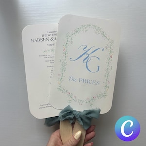 May include: Two cream-colored wedding fans with text and floral accents. One fan displays the names "KARSEN & C" and the date "May 17." The other fan features the initials "KG" and the words "The PRICES" in light blue. A teal ribbon bow adorns the wooden handles.