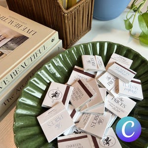 Peut inclure: Un bol vert rempli de boîtes d'allumettes blanches avec le texte "The Prices" imprimé dessus. Les boîtes d'allumettes sont décorées d'une bande brune et du texte "The Perfect Match" et "Wedding" imprimé dessus.