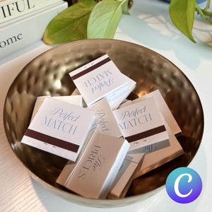 Peut inclure: Un bol en or rempli de boîtes d'allumettes. Les boîtes d'allumettes ont un fond blanc avec du texte bleu et brun. Le texte sur les boîtes d'allumettes indique "Perfect Match" et "The Prices".