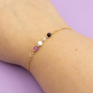 May include: A gold chain bracelet with purple, white, and black beads.