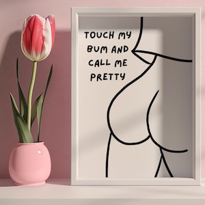 Pode incluir: Impressão emoldurada branca com uma arte de linha preta da parte de trás de uma pessoa. O texto "TOUCH MY BUM AND CALL ME PRETTY" está escrito em marcador preto.