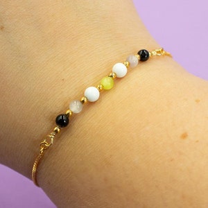 May include: A gold chain bracelet with black, white, and yellow beads.