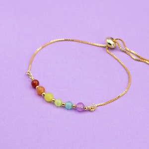 May include: A gold chain bracelet with a sliding clasp and a rainbow of coloured beads.