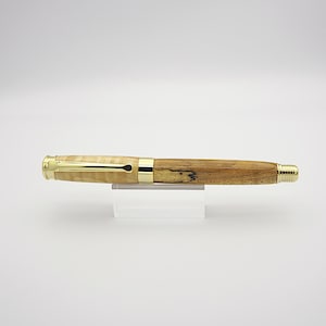 May include: A handcrafted wooden pen with a light-colored, patterned barrel and a darker, solid wood section. The pen features gold-colored metal accents and a gold-colored nib. The pen is displayed on a clear acrylic stand against a white background.