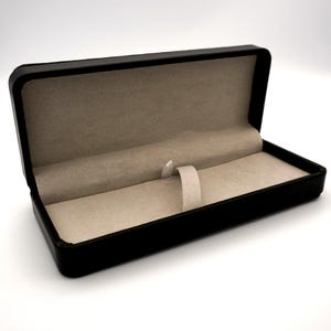May include: A black pen box with a beige interior and a pen holder. The rectangular box is open, revealing the soft lining and the pen holder. The exterior is a smooth, matte black.