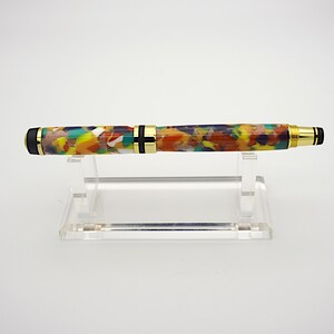 May include: A colorful, multi-colored pen with gold accents and black end caps. The pen is on a clear acrylic stand.