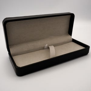May include: A black leather pen case with a gray felt interior and a white ribbon loop.