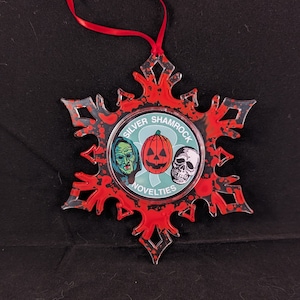 May include: A red and black snowflake ornament with a round, green, white, and black sticker featuring three faces. The sticker says "Silver Shamrock Novelties".
