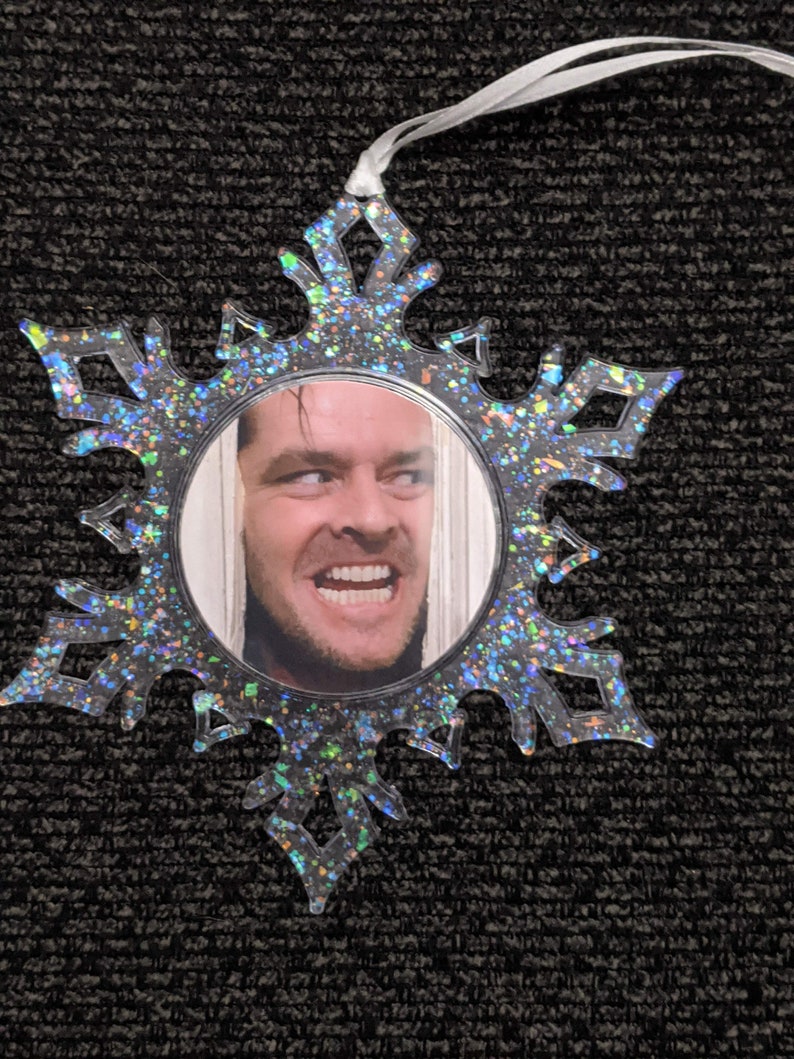 May include: A clear snowflake-shaped Christmas bauble with a glittery finish. The bauble features a round photo of a man with a surprised expression.