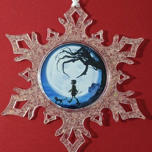 May include: A clear snowflake-shaped ornament with a glittery finish. The ornament features a round image of a child walking with a cat in a moonlit forest.