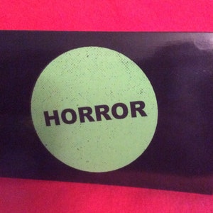 May include: A black and green card with a large green circle in the center. The circle has a distressed texture and the word "HORROR" printed in black letters.