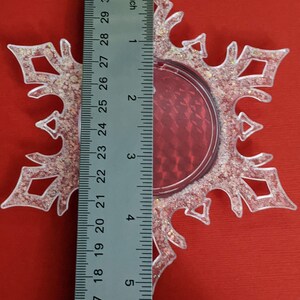 May include: A clear plastic snowflake ornament with a red glitter center. The ornament is approximately 3 inches in diameter.