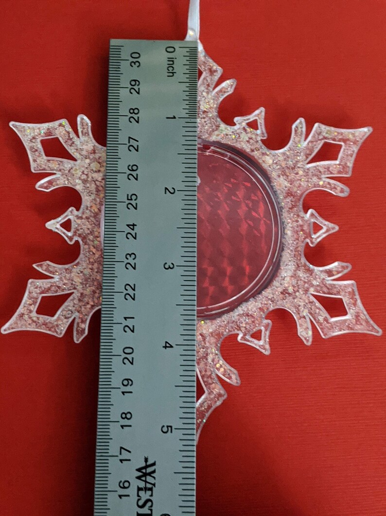 May include: A clear plastic snowflake ornament with a red glitter center. The ornament is approximately 3 inches in diameter.