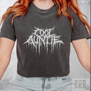 May include: A black cropped t-shirt with a white graphic that says "Cool Auntie" in a metal band font.