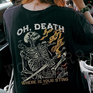 May include: Black t-shirt with a graphic print of a skeleton holding a sword. The text "Oh, Death Where Is Your Sting" is printed on the shirt.