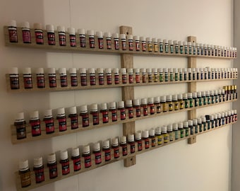 Puede incluir: Una estantería de madera con varias filas de pequeñas botellas de vidrio con tapas blancas. Las botellas están llenas de líquidos coloridos y están dispuestas en forma de arcoíris.