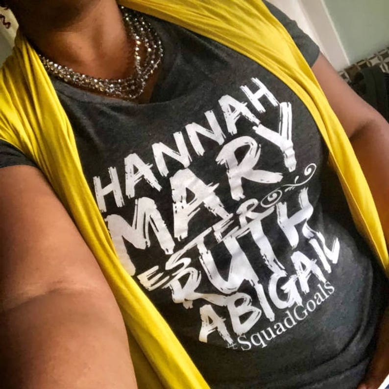 May include: A gray t-shirt with a yellow vest. The shirt has white text that reads "HANNAH MARY ESTHER RUTH ABIGAIL #SquadGoals".