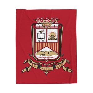 Op de afbeelding: Rode fleece deken met een gouden wapenschild met de letters "NAK" en de woorden "Nu Alpha Kappa" en "S.L.O."