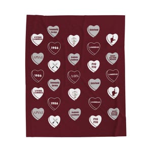 Puede incluir: Una manta de color burdeos con un patrón de corazones blancos. Cada corazón tiene un diseño diferente, incluyendo letras griegas, las palabras "Living Lambda", "FIU", "Sisterhood" y "1986".