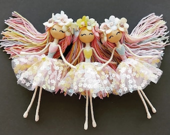 Peut inclure: Trois poupées en laine avec des bandeaux floraux et des jupes en tulle. Les poupées ont des visages peints et portent des couleurs pastel.