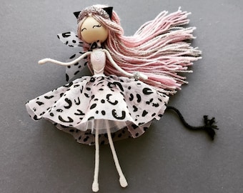 May include: A handmade doll with pink yarn hair, a black and white spotted dress, and black cat ears. The doll has a white wooden head and white yarn arms and legs.