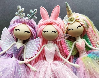 Peut inclure: Trois poupées faites à la main avec des cheveux en laine et des jupes en tulle. Les poupées sont habillées en licorne, en fée et en renne. La poupée licorne porte une jupe rose et blanche, la poupée fée porte une jupe violette et blanche et la poupée renne porte une jupe rose et blanche.