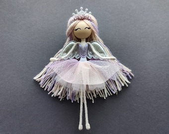 May include: A handmade doll with a pink and purple dress, silver wings, and a silver crown. The doll has yarn hair and a wooden head.