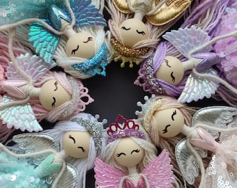 May include: A group of six handmade dolls with colorful wings and yarn hair. Each doll has a different color scheme and a unique design. The dolls are arranged in a circle, with their wings spread out.