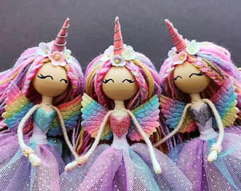 May include: Three handmade unicorn dolls with rainbow wings and tulle skirts. Each doll has a pink yarn mane and tail, a wooden head, and painted eyes and eyelashes.