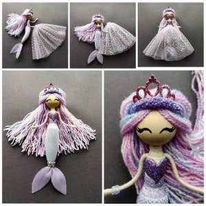 May include: A handmade mermaid doll with a purple and pink yarn hair, a sparkly purple bodice, and a white and purple tail. The doll is wearing a pink crown and has a painted face.