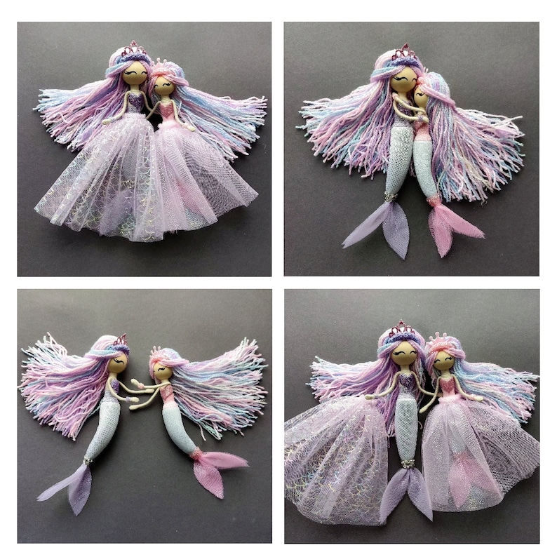 May include: Two handmade mermaid dolls with long, colorful yarn hair, wearing pink and purple tulle skirts and crowns. The dolls are holding hands and have painted faces.