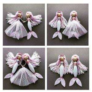 May include: Two pairs of handmade mermaid dolls with pink and purple yarn hair, wearing pink and white dresses and holding hands. The dolls have white and pink glitter tails.
