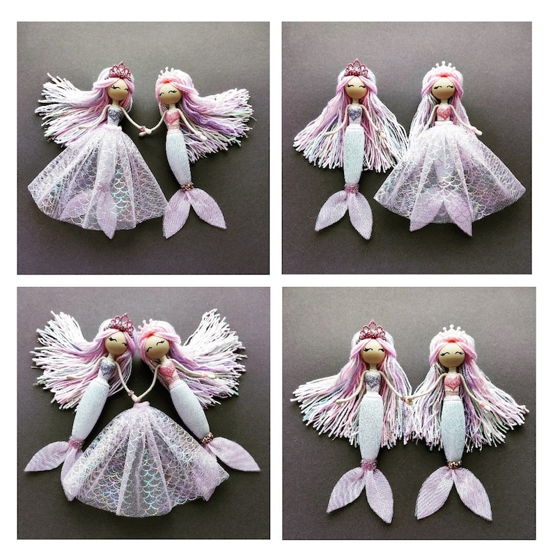 May include: Two pairs of handmade mermaid dolls with pink and purple yarn hair, wearing pink and white dresses and holding hands. The dolls have white and pink glitter tails.