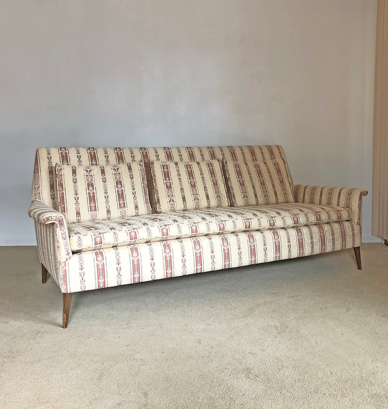 May include: A vintage striped sofa with a beige and brown patterned fabric. The sofa has three cushions and wooden legs.