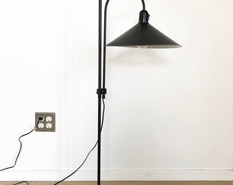 May include: A black floor lamp with a curved arm and a black shade. The lamp is on a black round base and has a black cord.