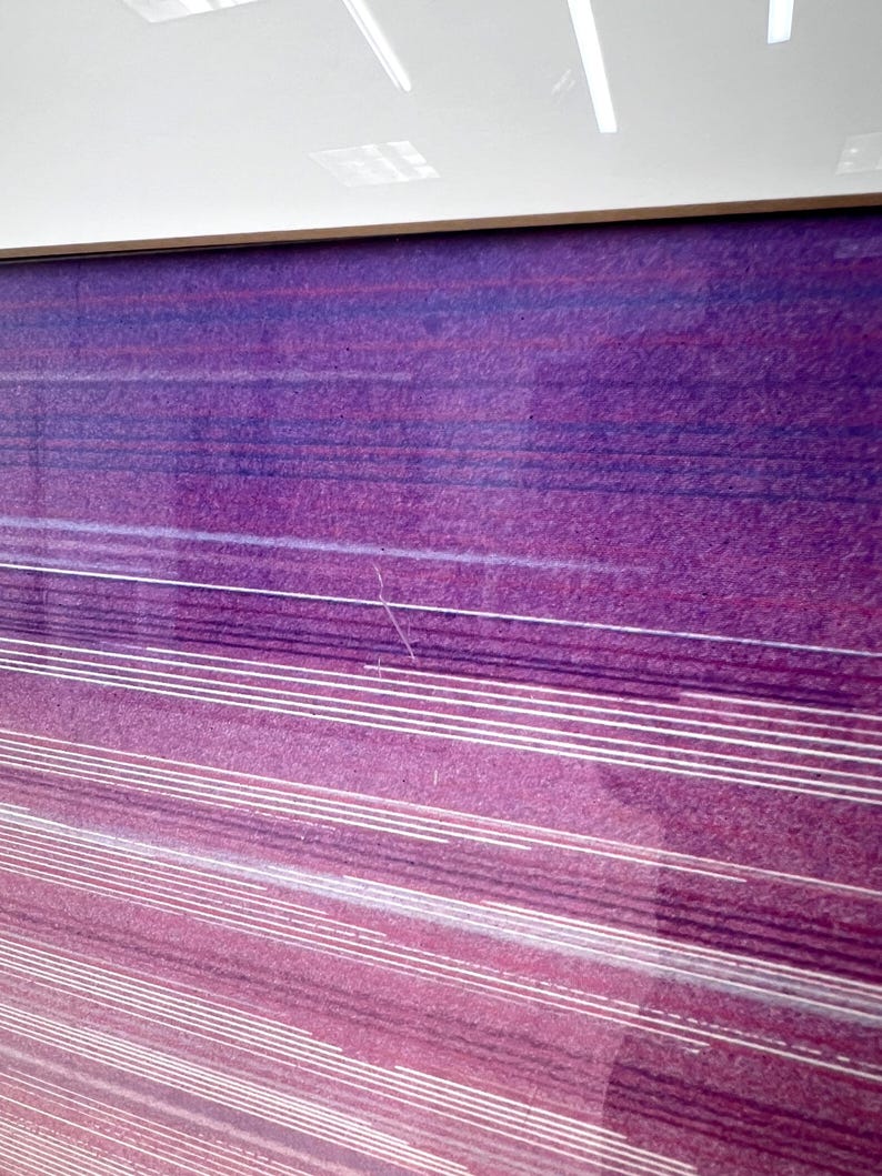 May include: Abstract art print with a gradient of purple and pink hues. Horizontal white lines create a sense of movement across the textured surface. The artwork is framed with a thin, light-colored border.