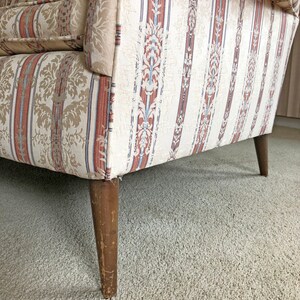 May include: A vintage striped sofa with a beige, brown, and blue patterned fabric. The sofa has wooden legs and is sitting on a beige carpet.