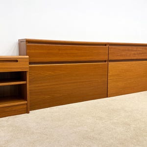 May include: A mid-century modern bedroom set in warm wood tones. The set includes a headboard with drawers and two nightstands with open shelving. The furniture has a clean, minimalist design.