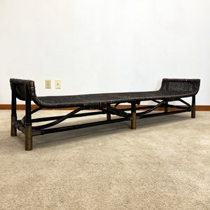 May include: A long, black wicker bench with a curved back and brass accents. The bench is sitting on a beige carpet.